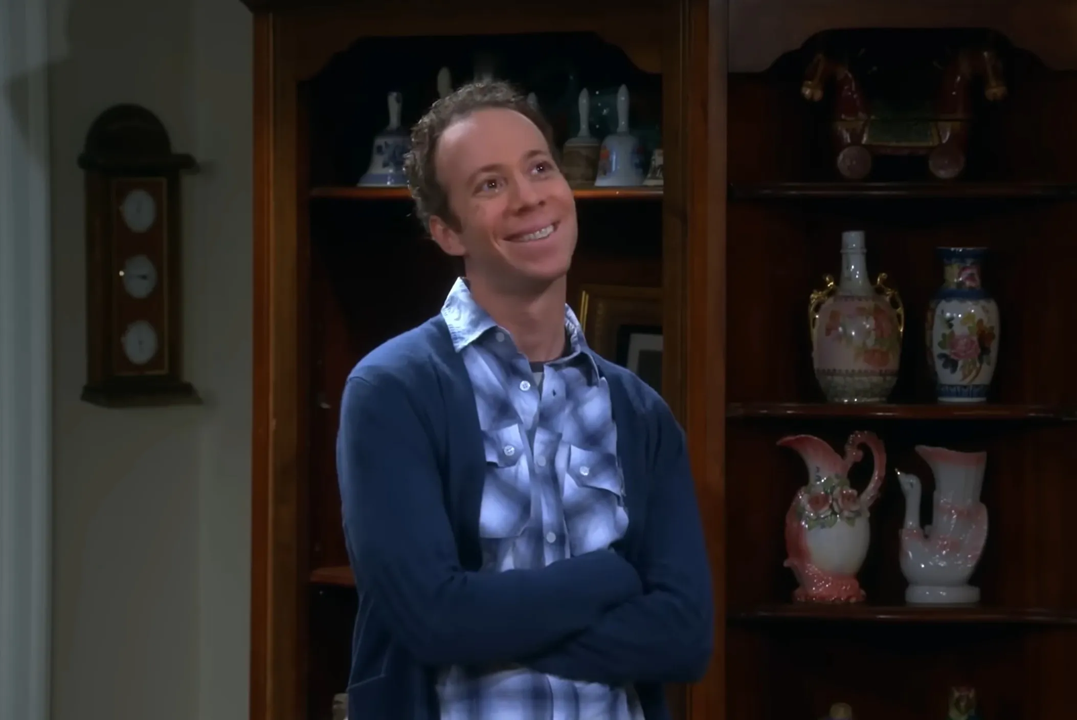 Stuart Bloom smiling with arms crossed in a living room setting from The Big Bang Theory TV show.