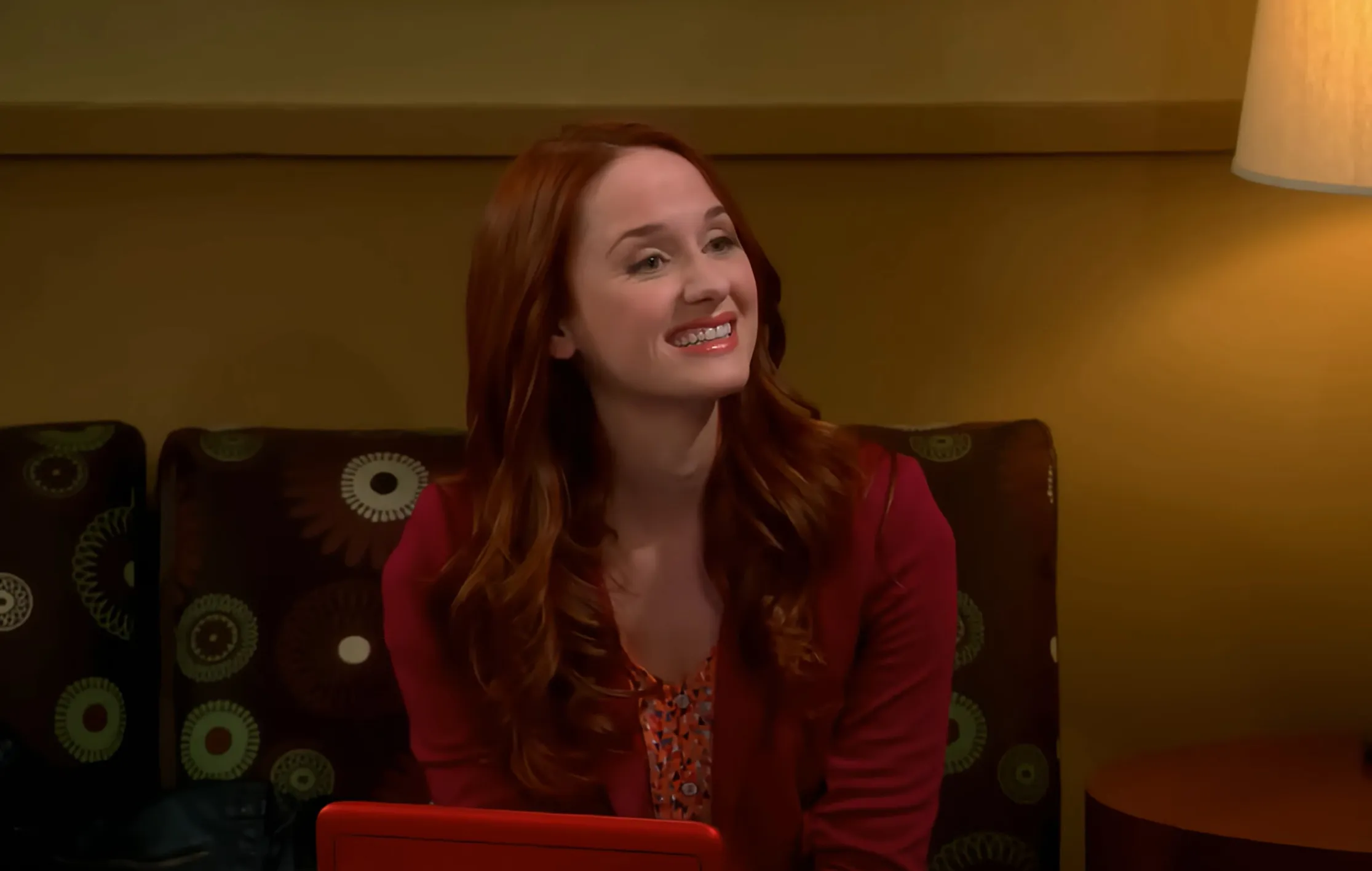Emily Sweeney smiling indoors, wearing a red blazer, representing the Comic Center of Pasadena in The Big Bang Theory.