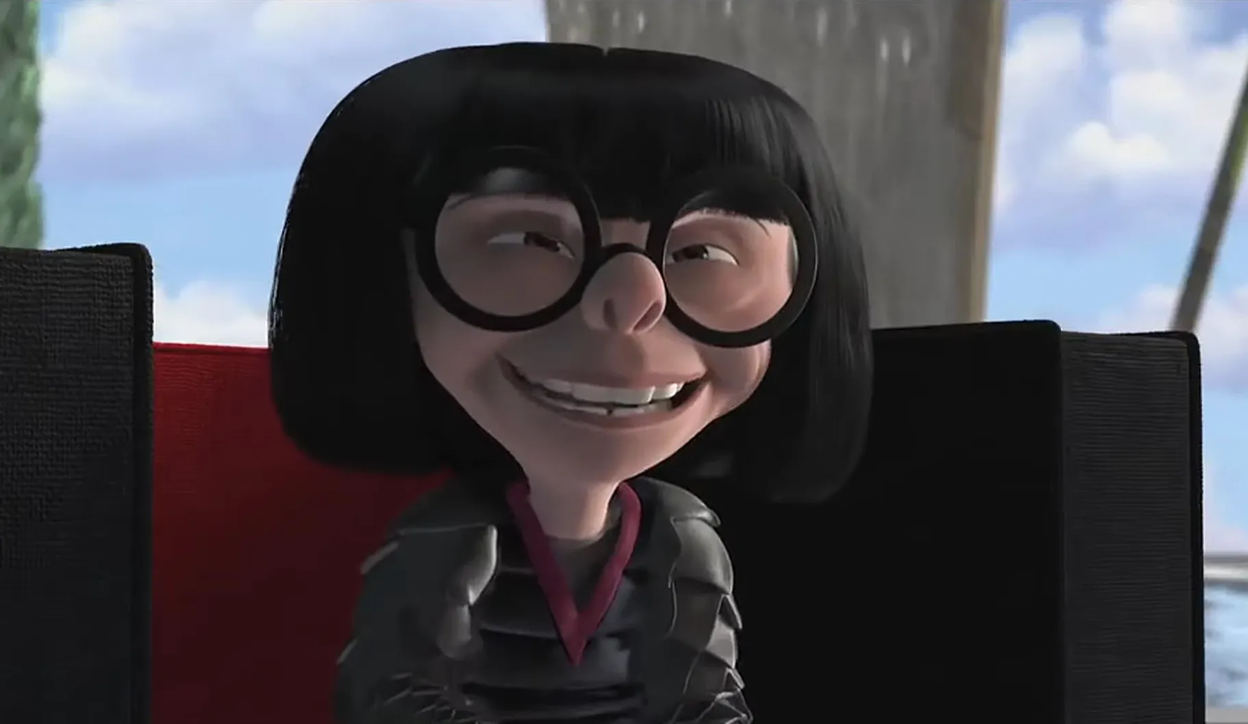 Supporting character from an animated film wearing round black glasses and a black outfit with a red collar, smiling indoors.