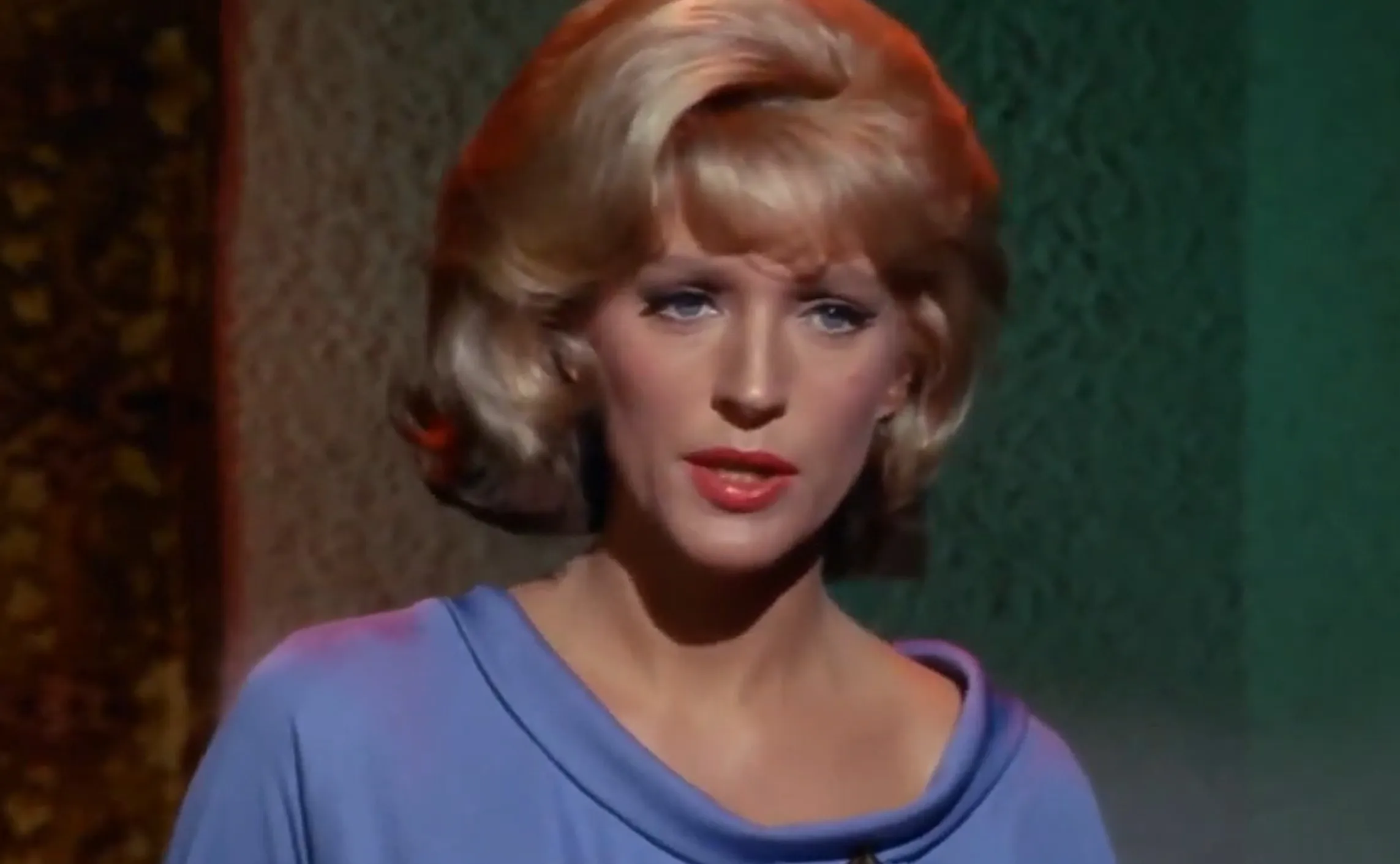 Close-up of Christine Chapel from Star Trek The Original Series with blonde hair and blue uniform top against patterned background