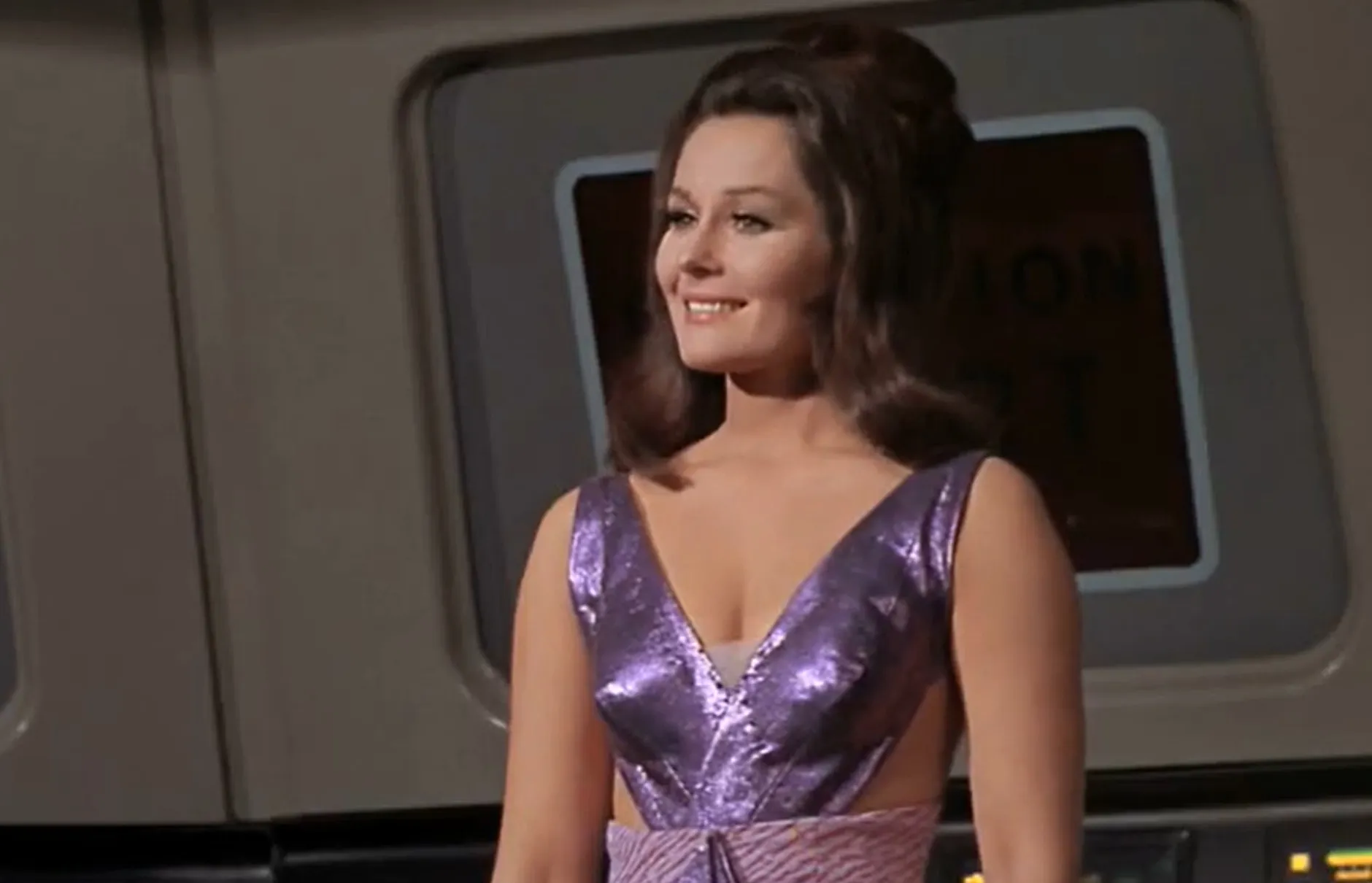 Christine Chapel from Star Trek The Original Series smiling in a shiny purple dress aboard a spaceship interior.
