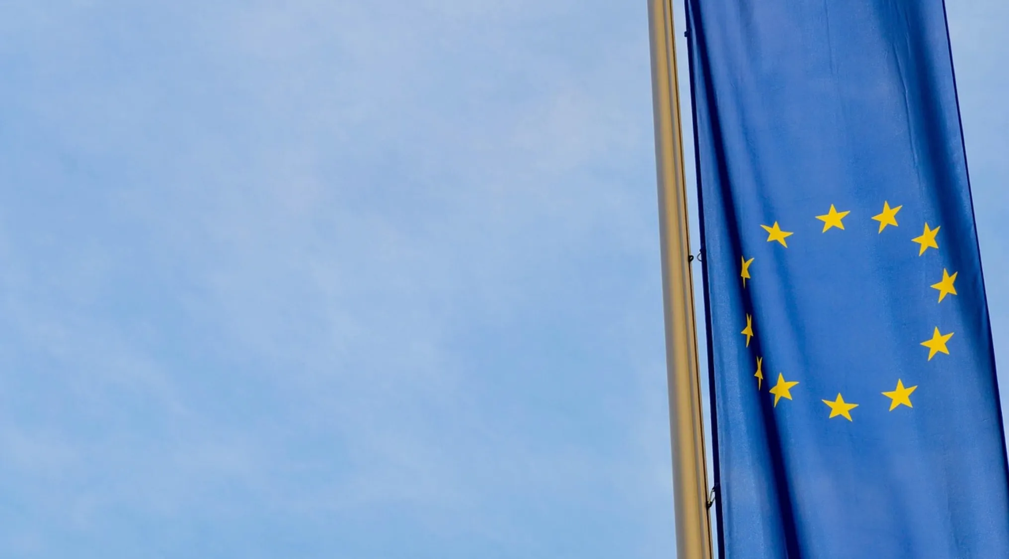 European Union flag waving on a pole against a clear blue sky representing geography quiz on EU countries.