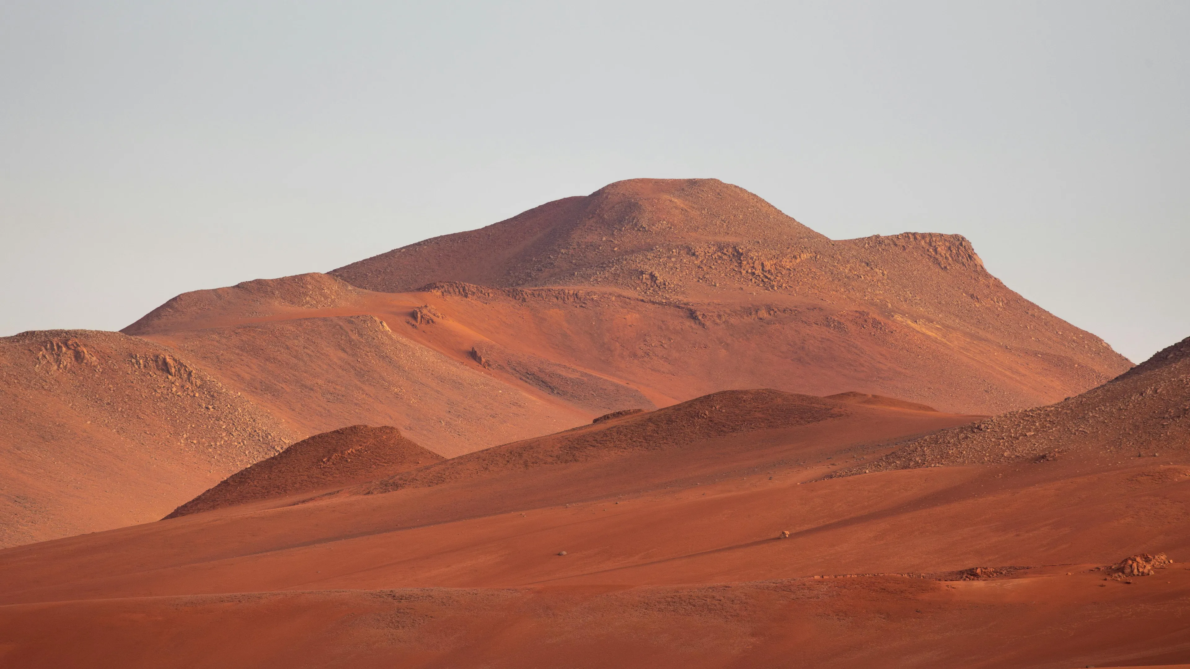 Arid reddish-brown hills in Chile’s Atacama Desert under clear sky, showcasing desert geography and terrain features.