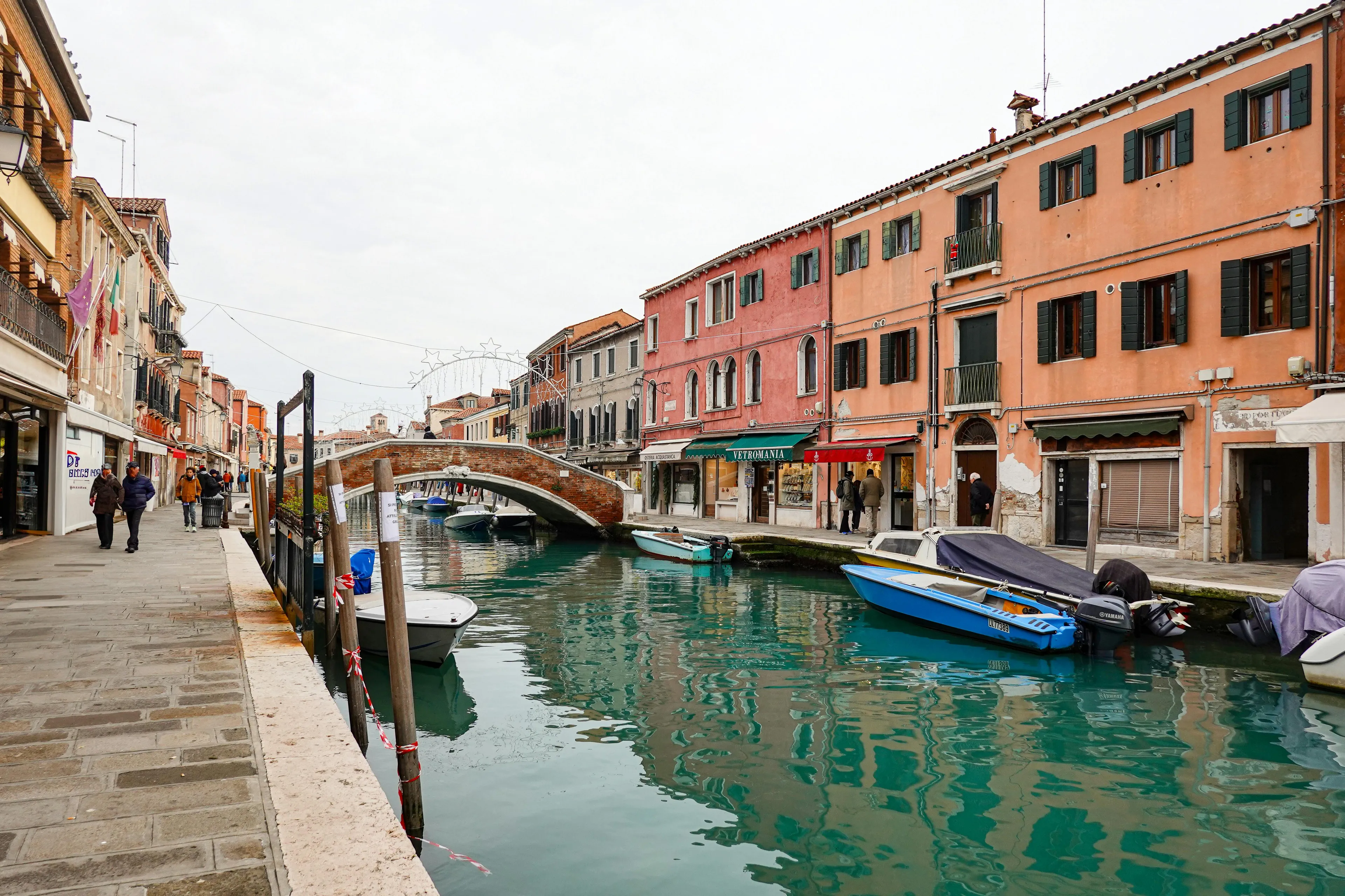 Canal in Venice with boats and historic buildings reflecting in water during acqua alta high tide flooding.