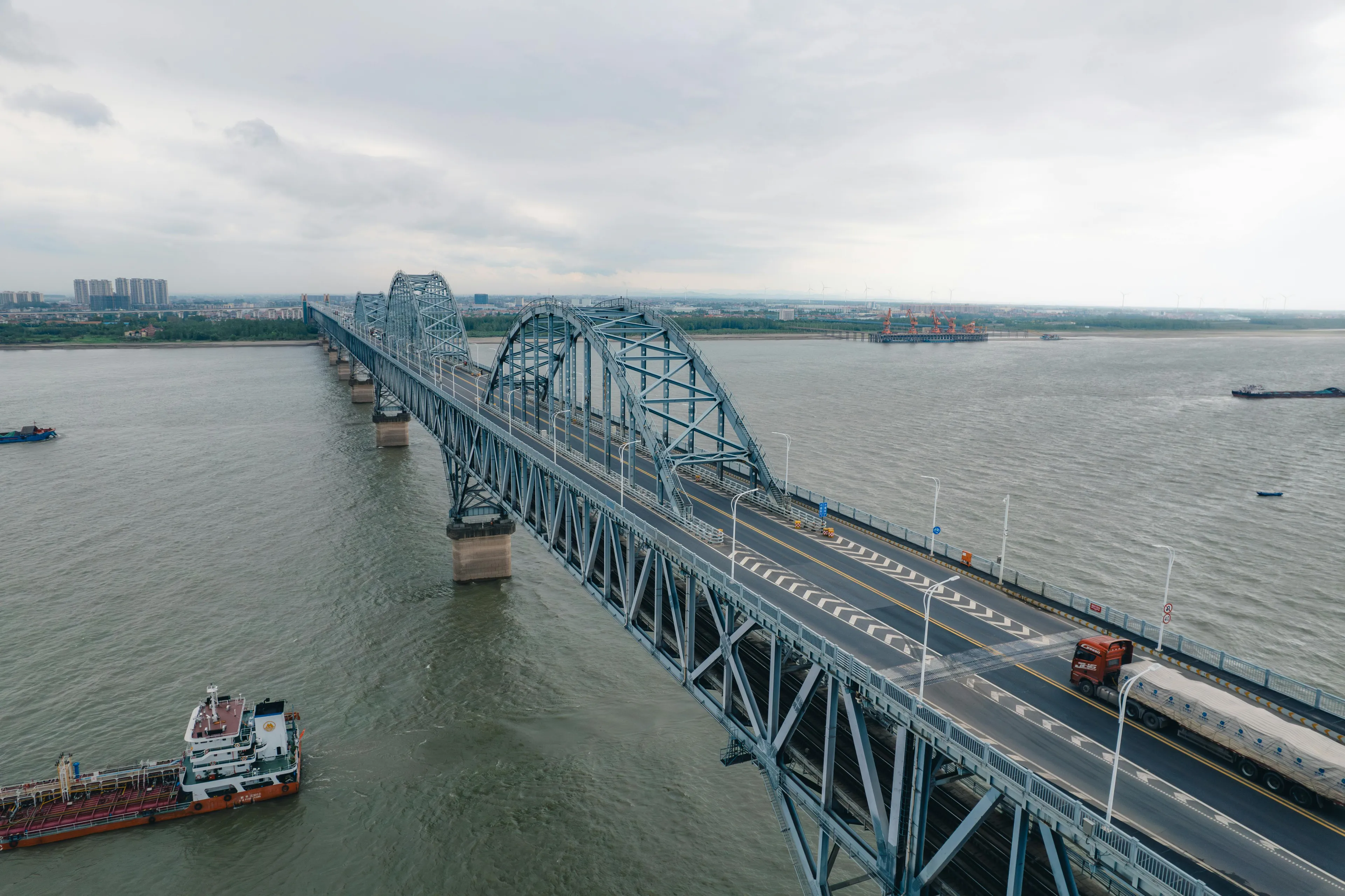 Steel arch bridge over the Yangtze River in China with vehicles and boats under cloudy sky landscape.