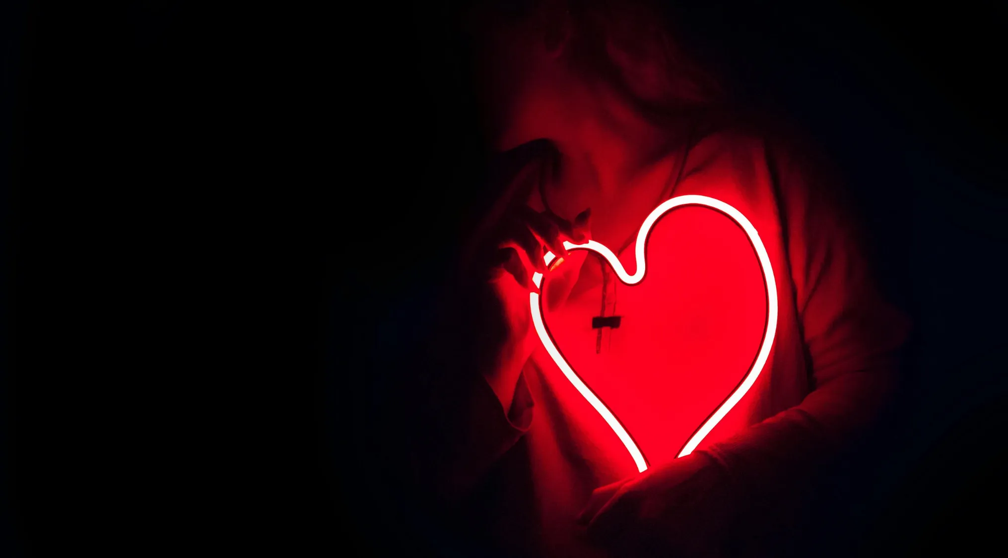 Person holding a glowing red neon heart in a dark room, symbolizing love in the alphabet combo quiz context.