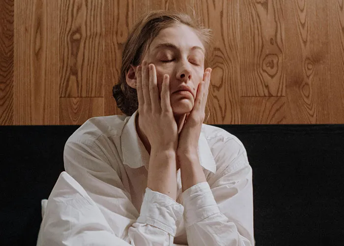 Woman in white shirt with tired expression touching her face, illustrating common medical issues affecting daily life.