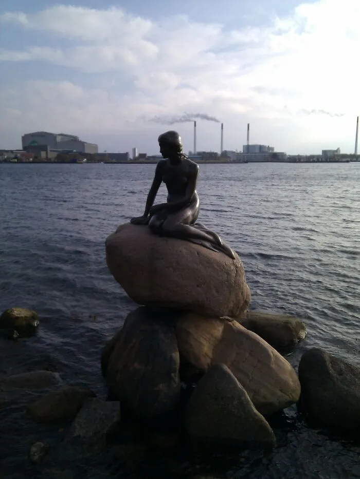 Bronze mermaid statue sitting on rocks by the waterfront, a well-known disappointing tourist attraction in the city.
