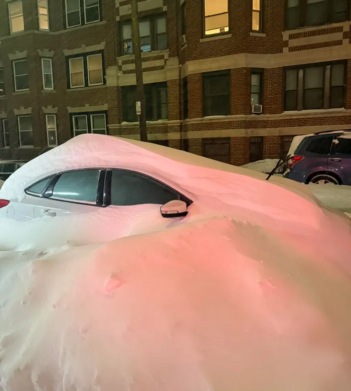 Car covered in snow during a heavy snowstorm in the U.S. with a brick apartment building in the background at night
