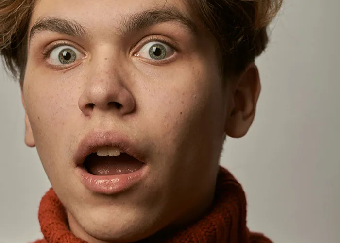 Young man with a shocked expression sharing a wacky story, hoping someone will believe his surprising experience.