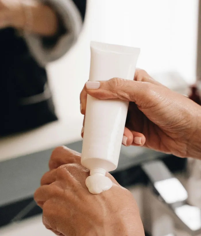 Hands applying lotion from a white tube on bathroom sink, friends family weird theme