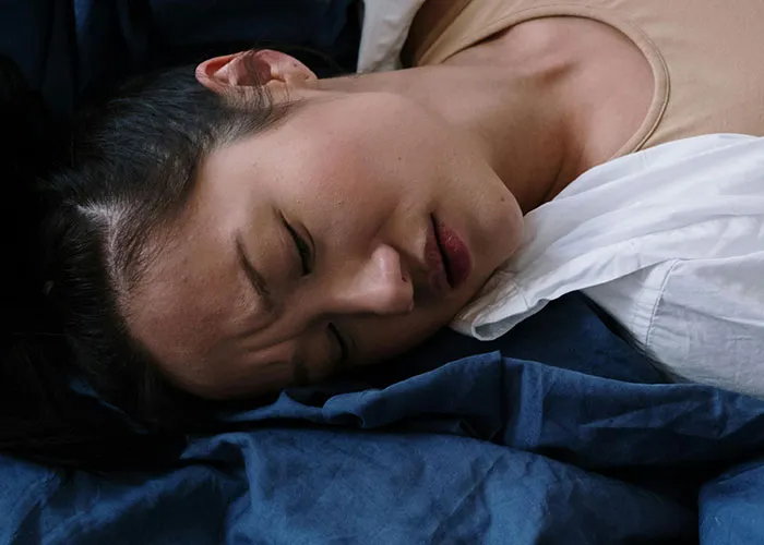 Young woman lying down with a pained expression, illustrating severe medical issues and discomfort.