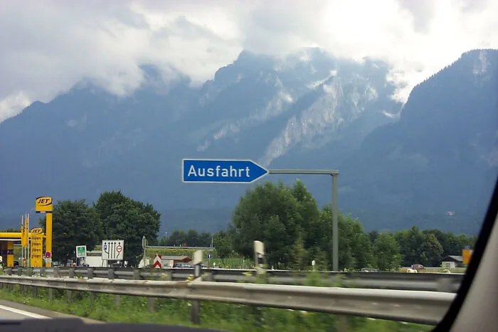 Highway exit sign in German with mountainous landscape, illustrating local inside jokes shared by people.
