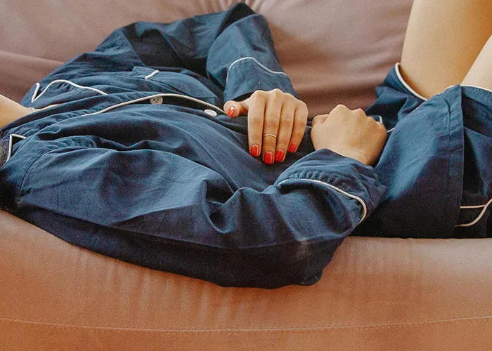 Person lying on a couch in blue pajamas, showing signs of distress related to medical issues and health struggles.