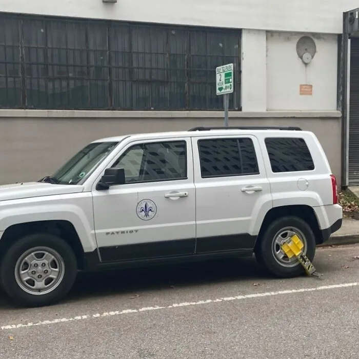 White SUV parked on the street with a yellow wheel lock in place, one of the weirdest things found in the streets.
