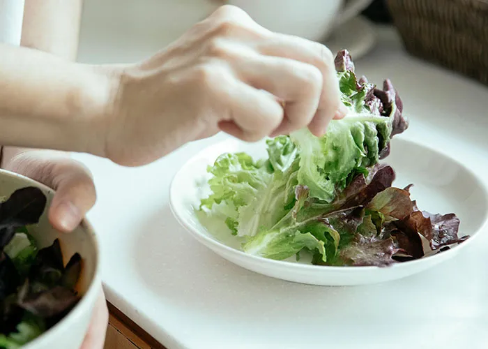 Person preparing a fresh salad with leafy greens, illustrating healthy eating advice from medical professionals.