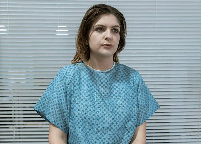 Young woman in a medical gown sitting in a clinic, reflecting on the worst things medical professionals have said to patients