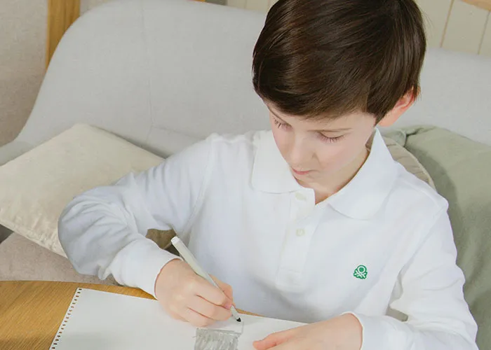 Young boy in white shirt drawing on paper at a table, capturing kids with no filter revealing family lore.
