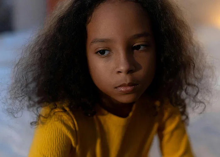 Young girl with curly hair wearing yellow, looking thoughtfully away, illustrating kids with no filter sharing family lore stories.