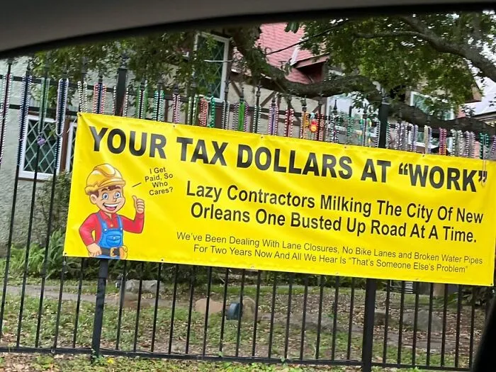 Yellow protest banner criticizing lazy contractors and street repairs, highlighting weirdest things found in the streets.