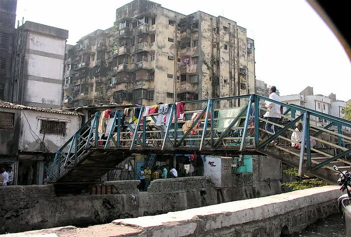 Worn pedestrian bridge with clothes drying on rails in front of aging apartment buildings, disappointing tourist attractions scene.