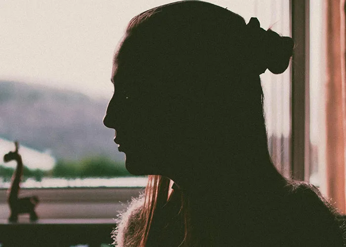Silhouette of a woman indoors by a window, reflecting on emotions related to discovering not being a biological parent.