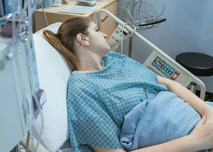 Woman in hospital gown lying in bed receiving medical treatment for serious medical issues in a clinical setting