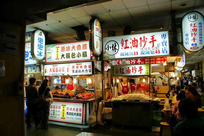 Indoor night market food stalls with bright signs, crowds, and vendors offering local dishes at disappointing tourist attractions.