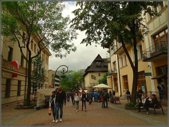 Crowded street with tourists and locals walking and sitting near buildings at a disappointing tourist attraction site.