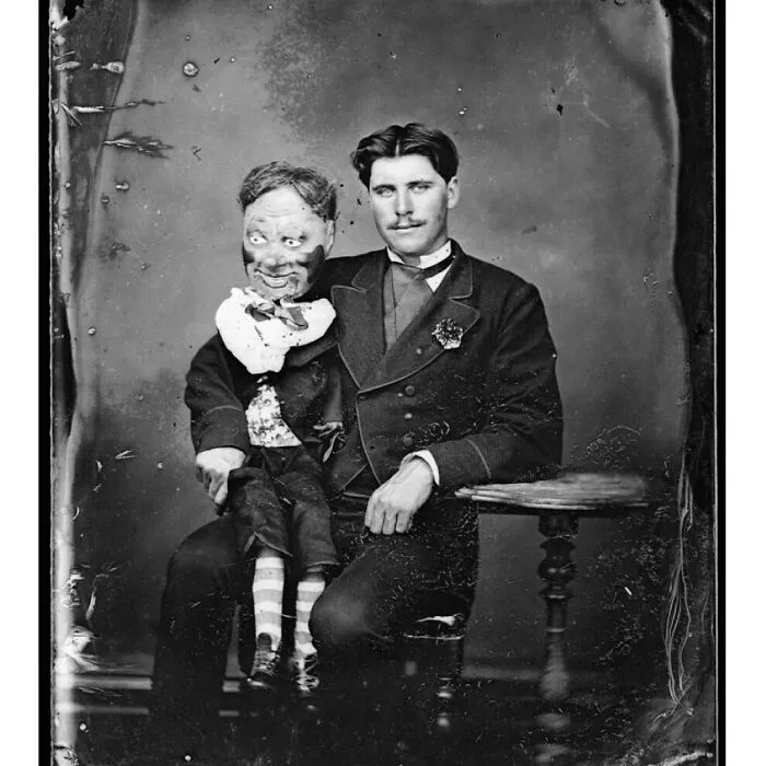 Vintage black and white photo of a man seated with an odd and creepy ventriloquist dummy on his lap.