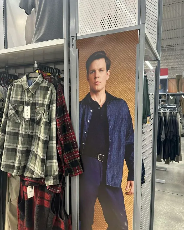 Store display featuring a poster of a man next to hanging flannel shirts, evoking memes inspired by The Office TV series.