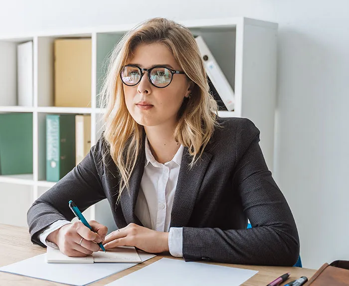 Young professional woman in glasses and business suit taking notes during a job interview with recruiters in office.