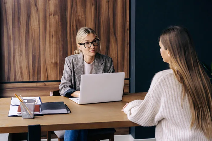 Recruiter in glasses with laptop interviewing a job candidate in a professional office setting about job applications.