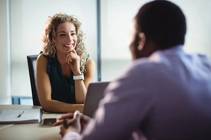 A female recruiter smiling and engaged during a job interview with a male candidate in a professional office setting.