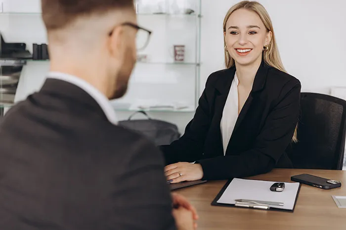 A female recruiter smiling and interviewing a male job candidate in a modern office setting.