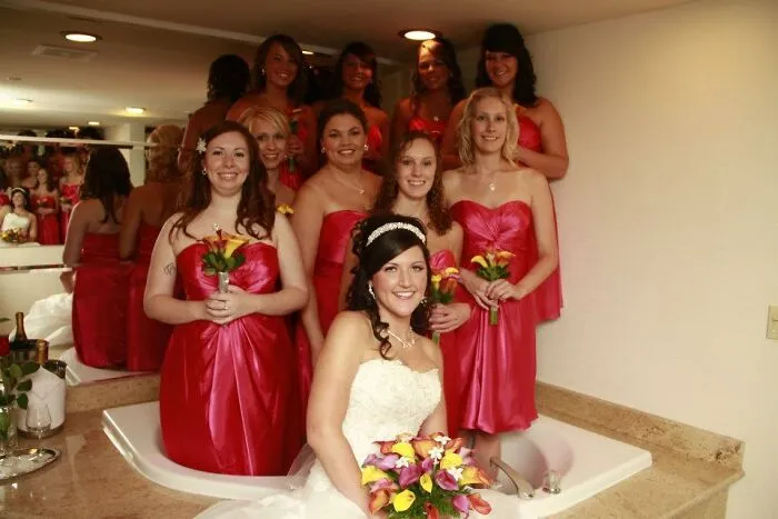Novia y damas de honor con vestidos rojos posando en una bañera en fotos de bodas divertidas y memorables.