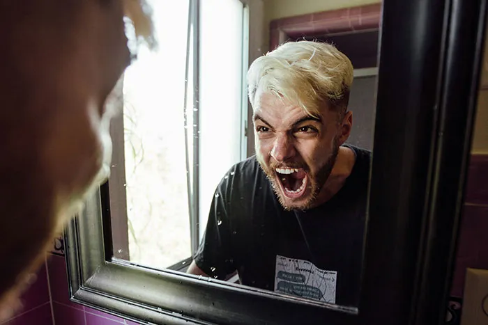 Man with platinum blonde hair shouting aggressively at his reflection, highlighting things men want women to understand.