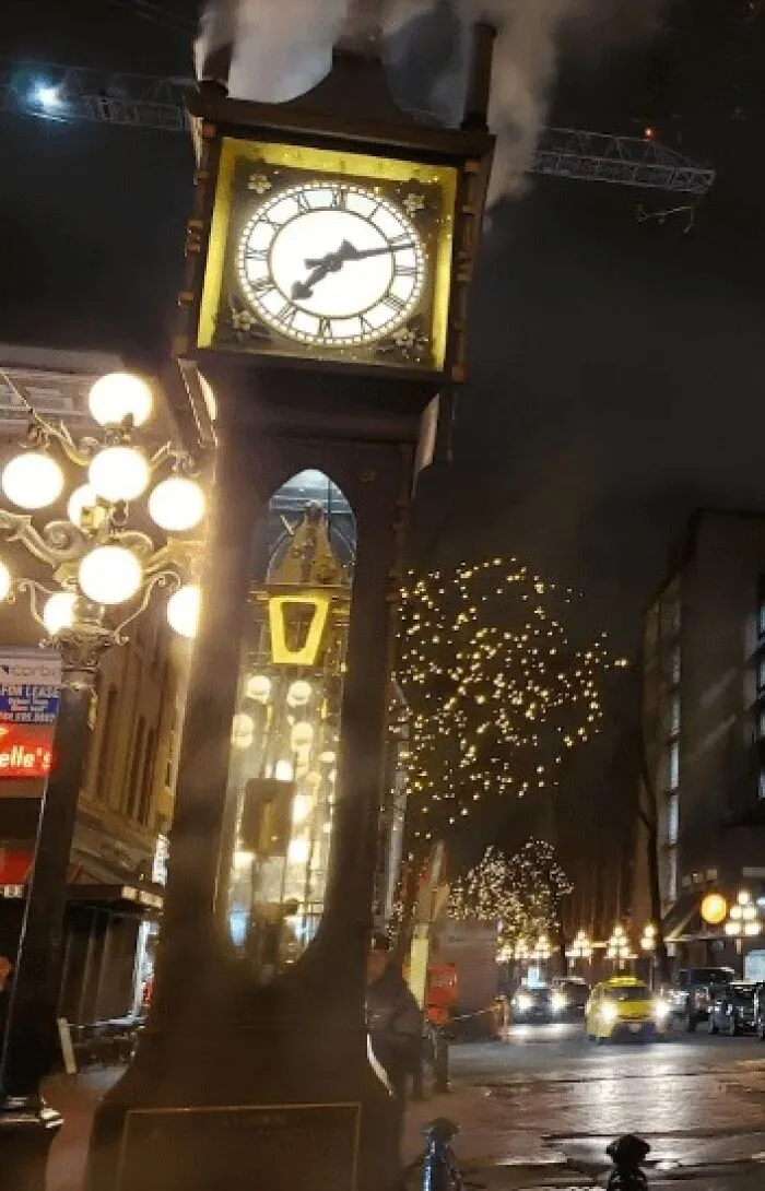 Steaming clock tower lit at night with street lamps and festive lights, a disappointing tourist attraction locals still don’t get.