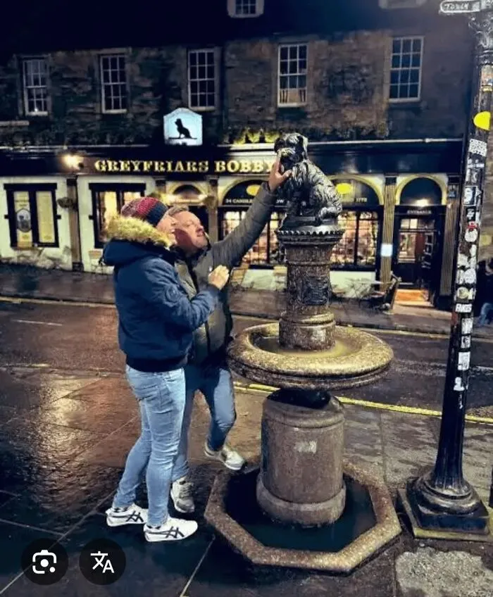 Two tourists at the Greyfriars Bobby statue touching the dog in a well-known but disappointing tourist attraction.