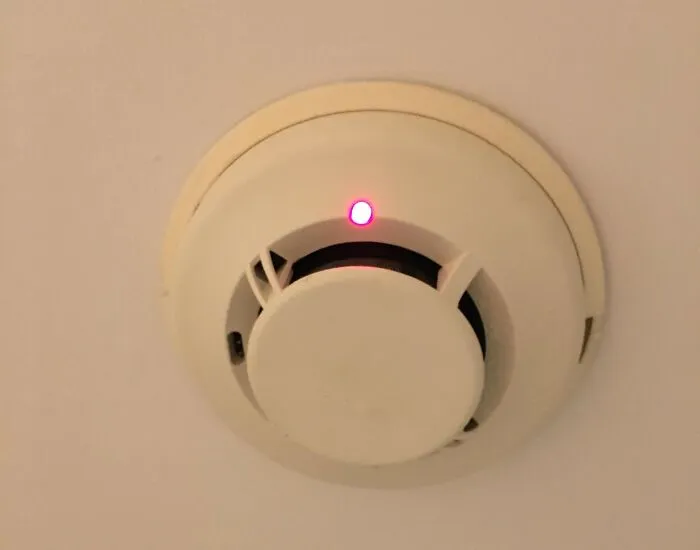 Smoke detector with a red indicator light installed on the ceiling, relevant to shipping containers safety solutions.