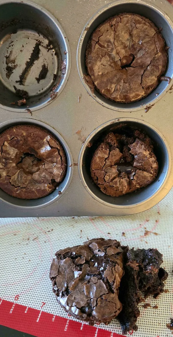Cracked and broken brownies in a muffin tray with one piece crumbled on a baking mat showing dessert ruined attempts.