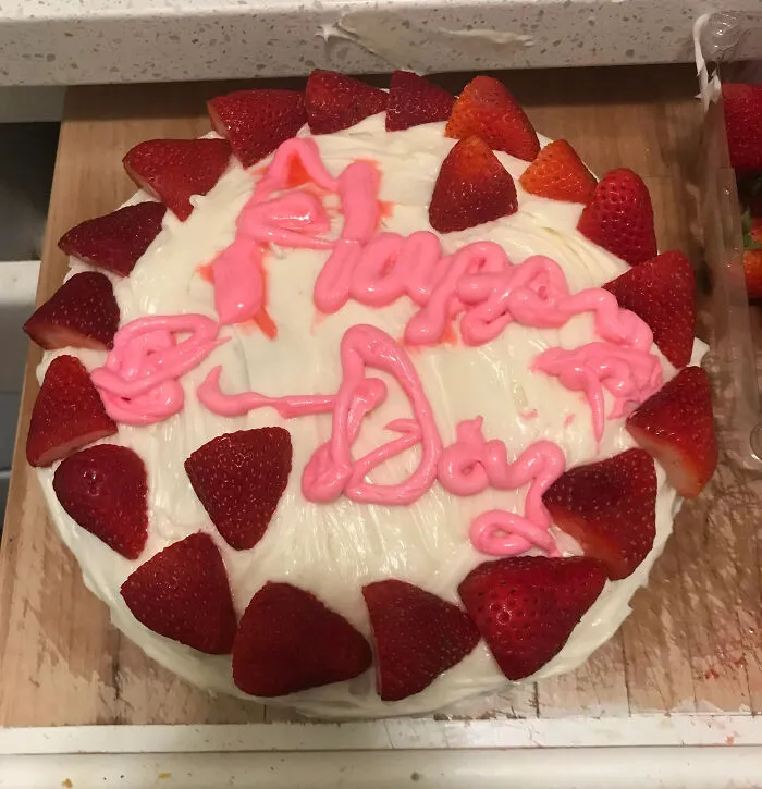 Cake with uneven pink icing text and strawberry decoration showcasing a dessert ruin fail.