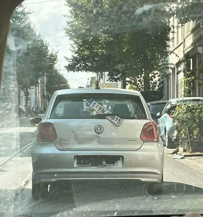 Silver Volkswagen Polo with a misplaced license plate hanging inside the rear window on Brussels streets, showcasing weird street scenes.