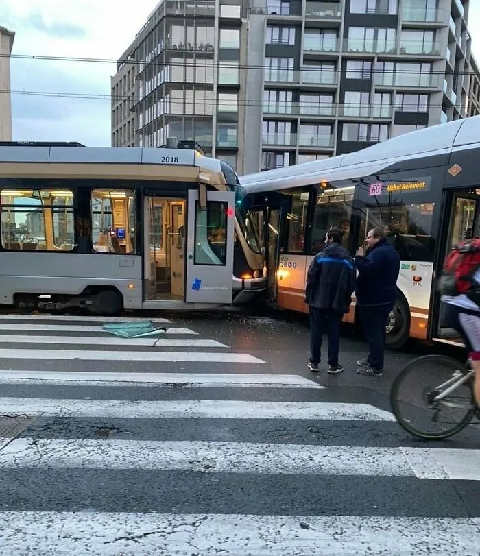 Collision between tram and bus on a busy street in Brussels with pedestrians and cyclist nearby.