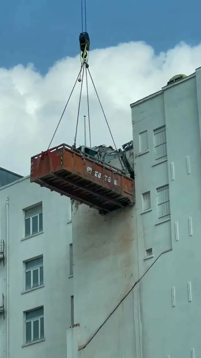 A large construction container being lifted by a crane on the streets of Brussels in an unusual scene.