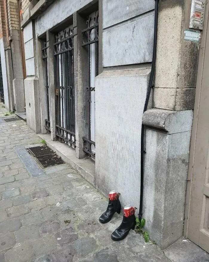 Black boots filled with crushed soda cans placed on a cobblestone street in Brussels, showcasing weirdest street sighting.