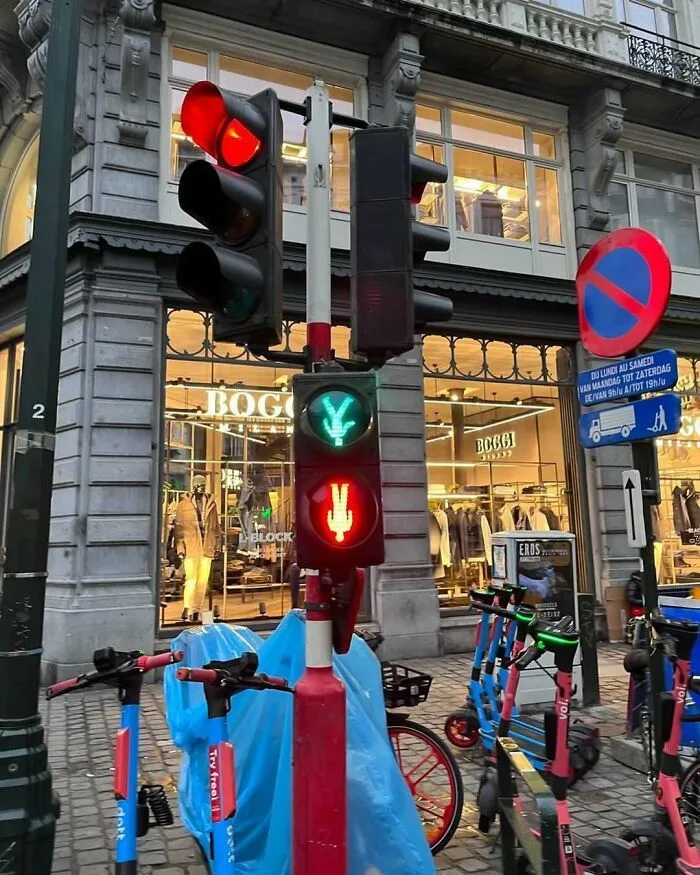 Unusual traffic light with green and red peace sign signals on a busy street in Brussels with scooters parked nearby.