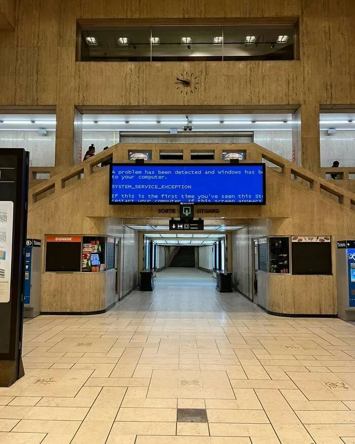 Public space in Brussels showing a large digital screen with a blue error message, illustrating weird and unhinged street scenes.