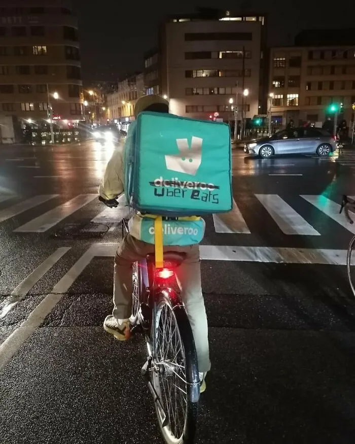 Food delivery cyclist in Brussels with edited delivery bag showing strange and unhinged street scene at night.