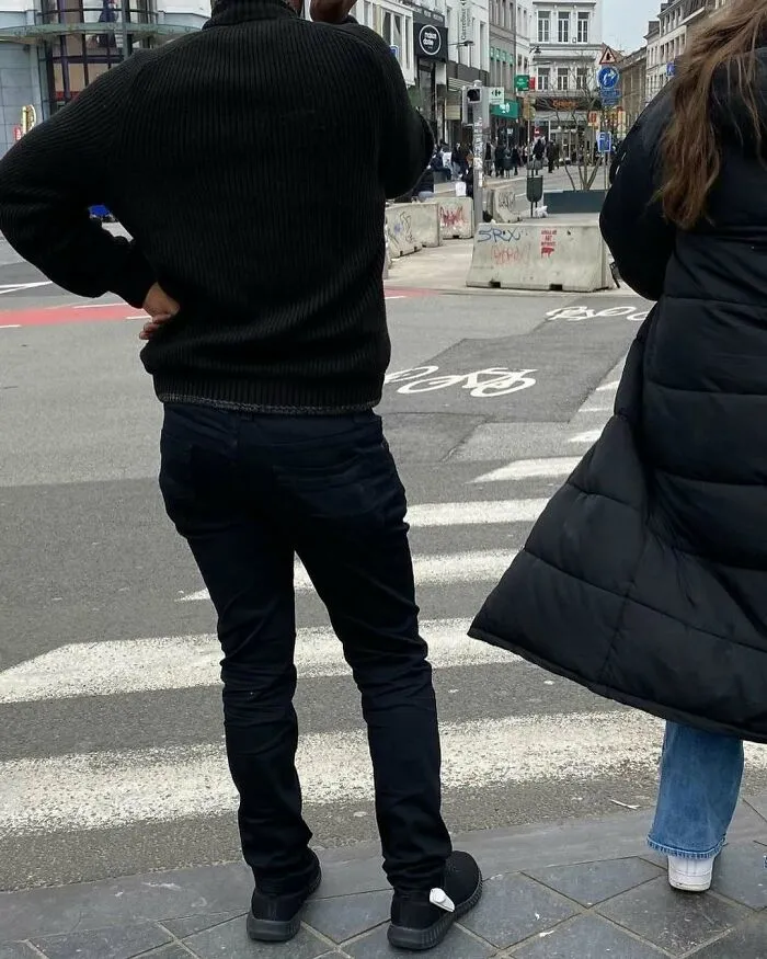 Two people standing at a crosswalk on the streets of Brussels showing weird and unhinged urban street scenes.